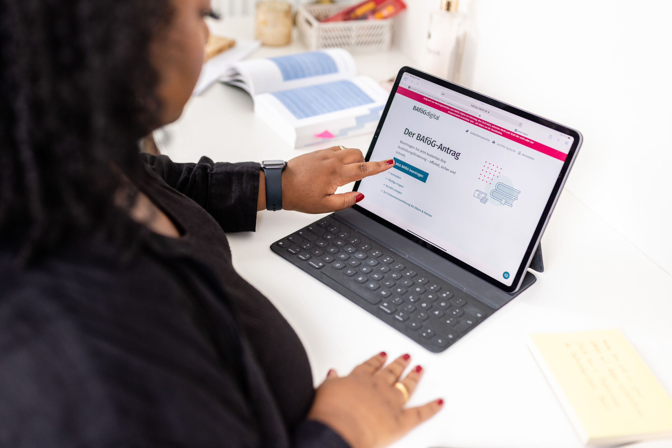 A person clicks on a tablet with the BAFÖG-digital website open, selecting ‘Apply’