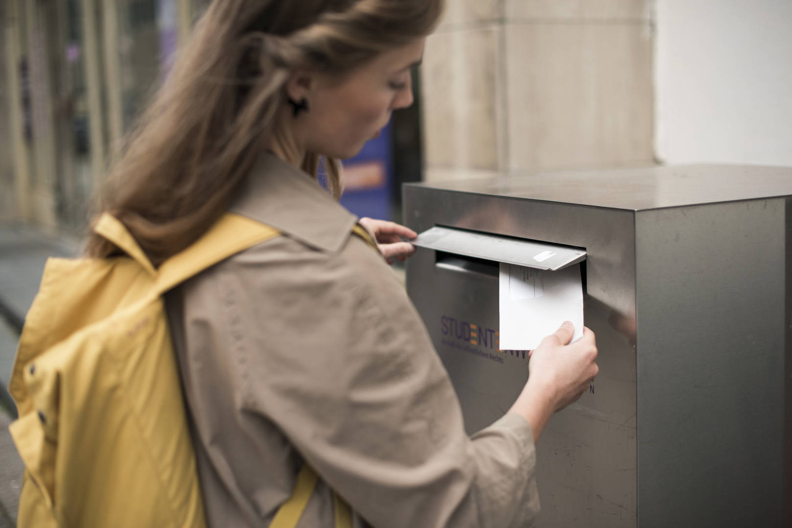 A student posts a letter in a postbox