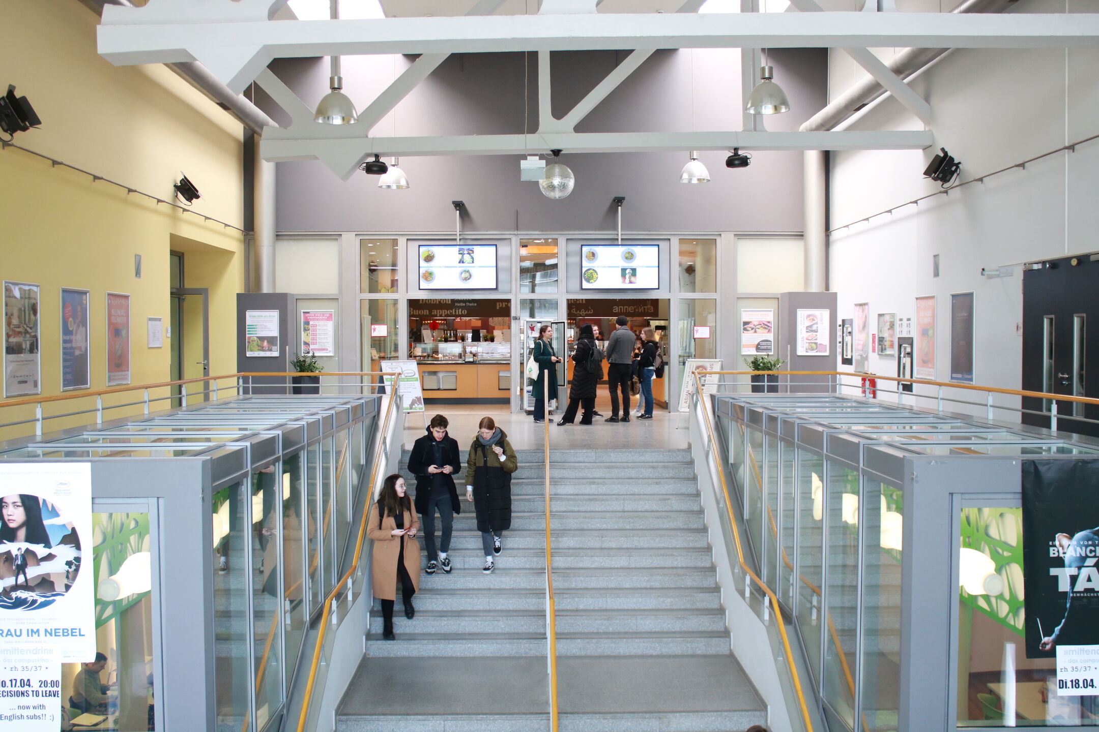 The cafeteria lobby, stairs with students, poster frames on the walls
