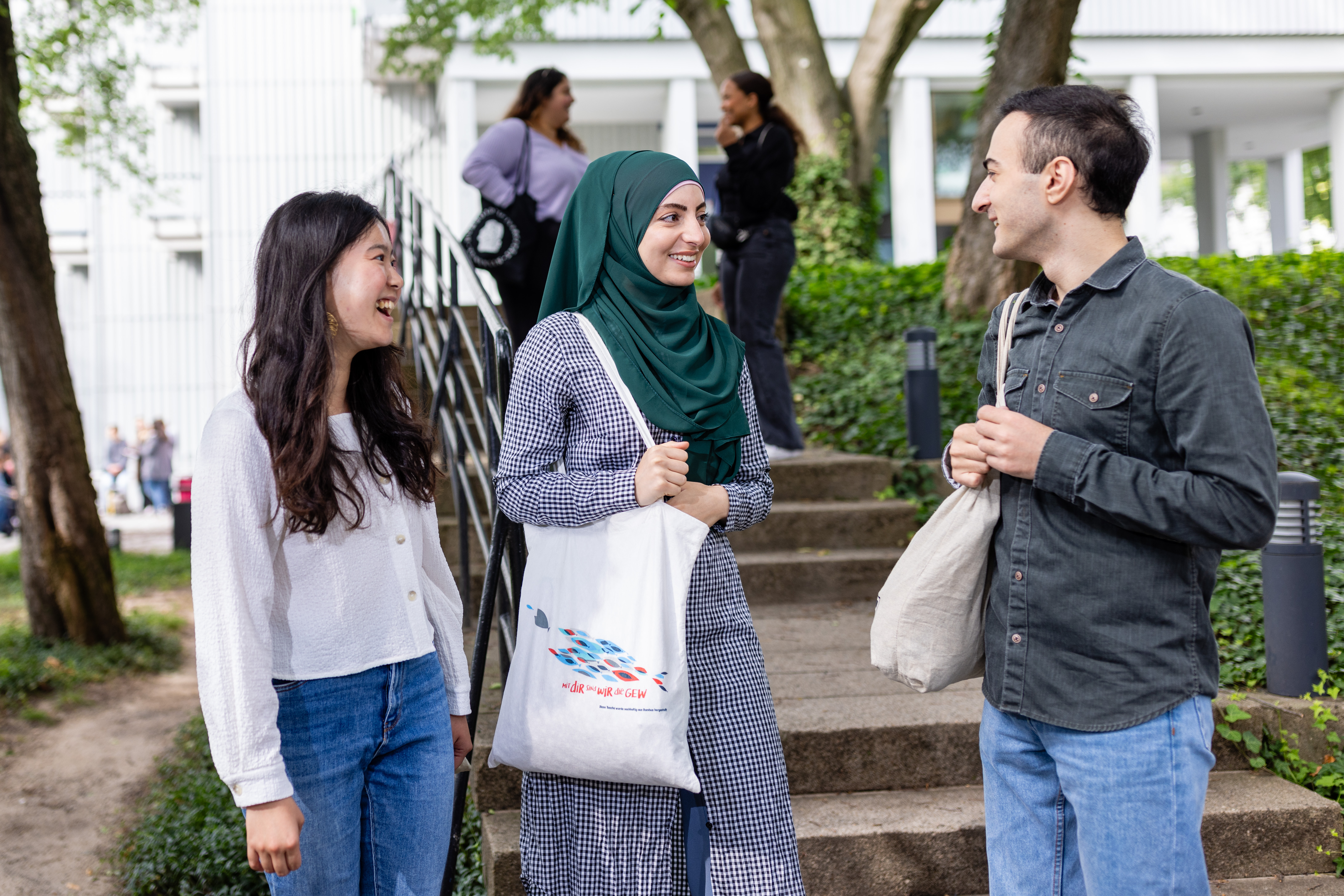 Two female international students (one of whom is wearing a headscarf) and a male international student are chatting outdoors