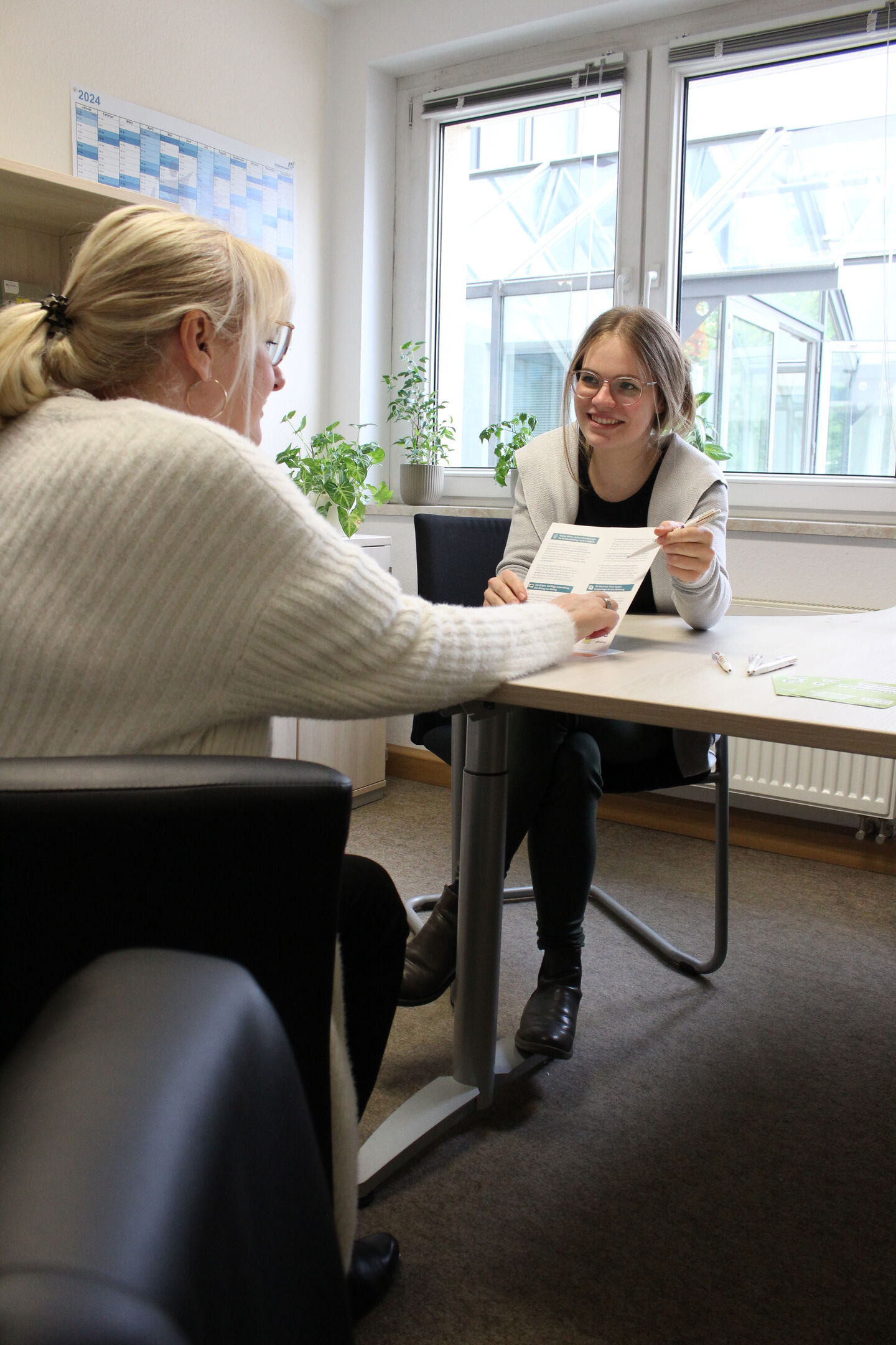 lächelnde Frau zeigt auf einem Blatt etwas und eine Kundin sitzt ihr gegenüber