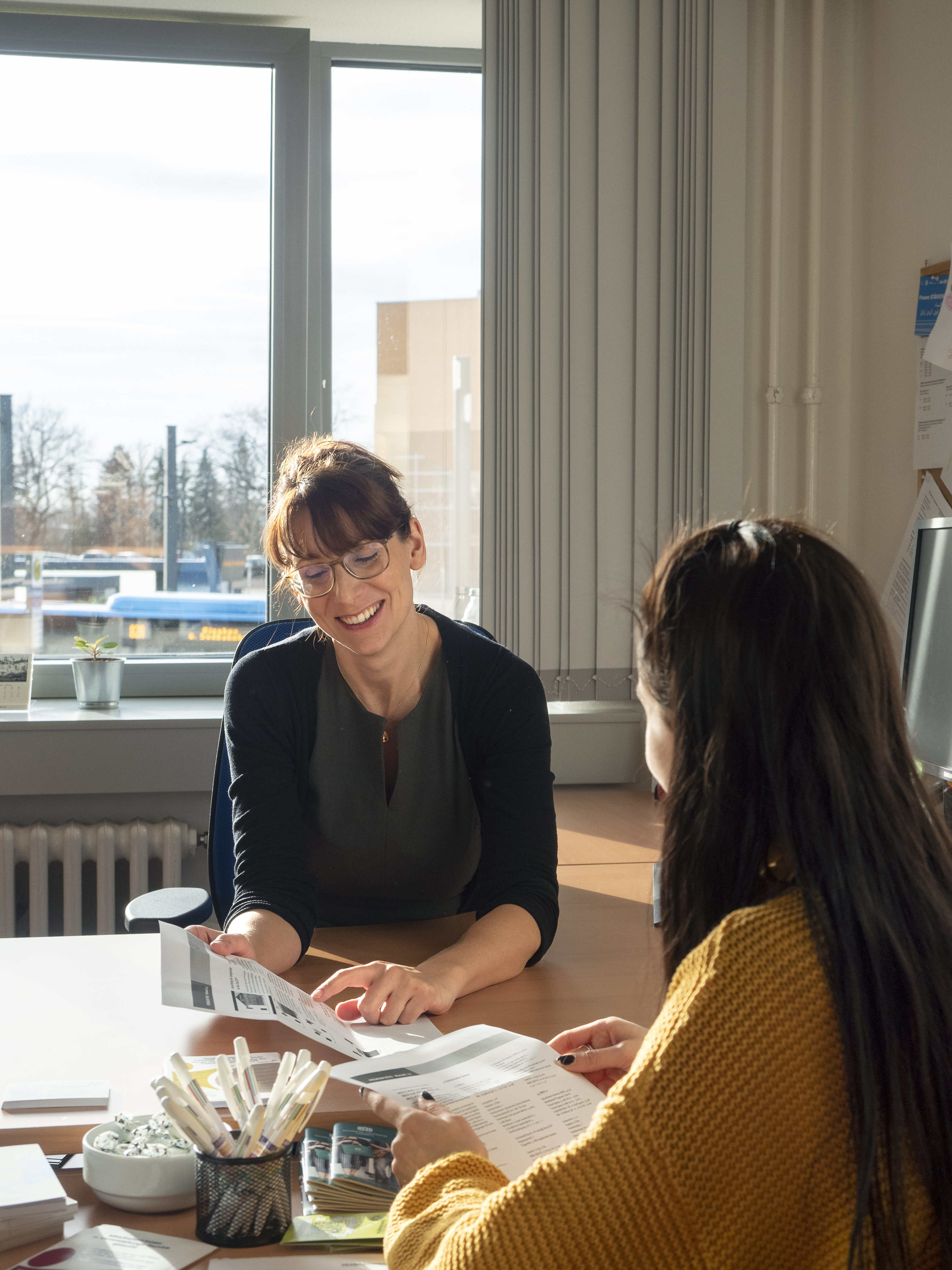 Consultation around a table; a smiling woman is pointing at something on a sheet of paper