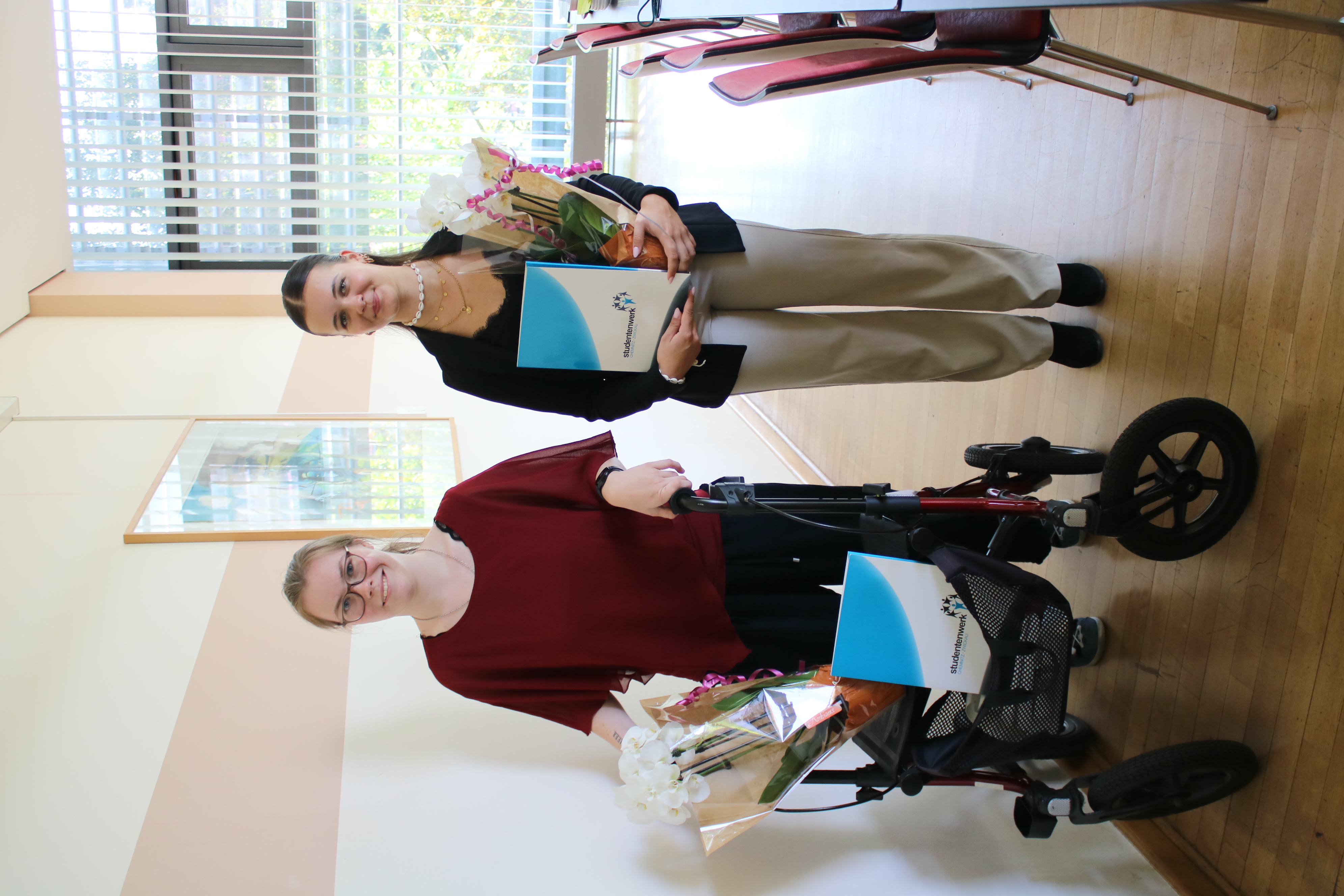 Two female skilled workers at their graduation ceremony, holding flowers and certificates