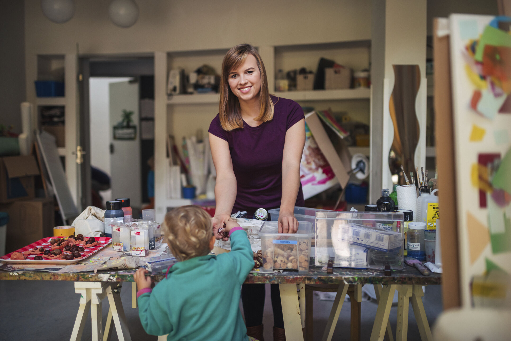 A member of staff at the daycare centre is standing in front of a table set out with art supplies for the children