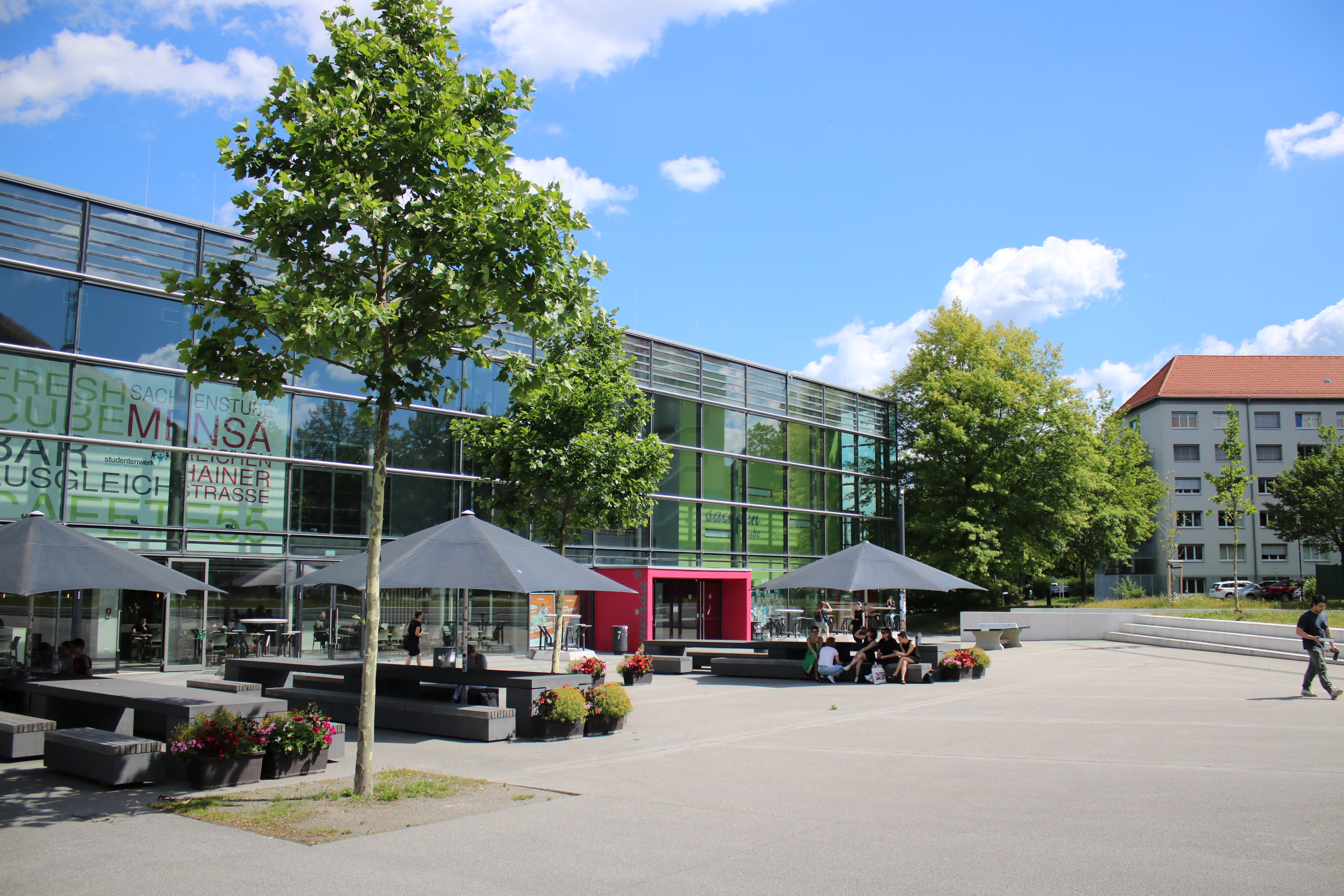 Gebäude mit Glasfassade, davor offene Sonnenschirme mit Sitzmöglichkeit