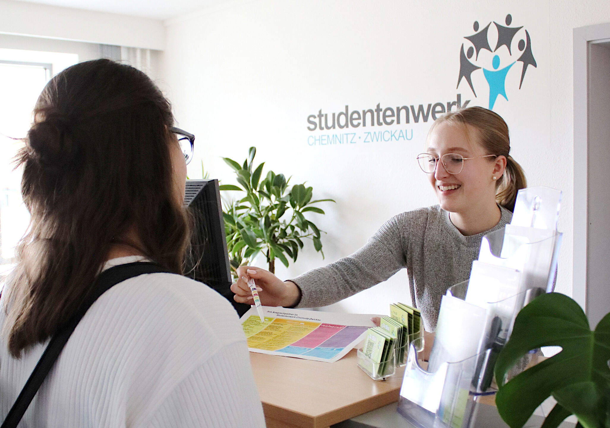 freundliche Person am Infopunkt erklärt einem Studierenden unsere Dienstleistungen