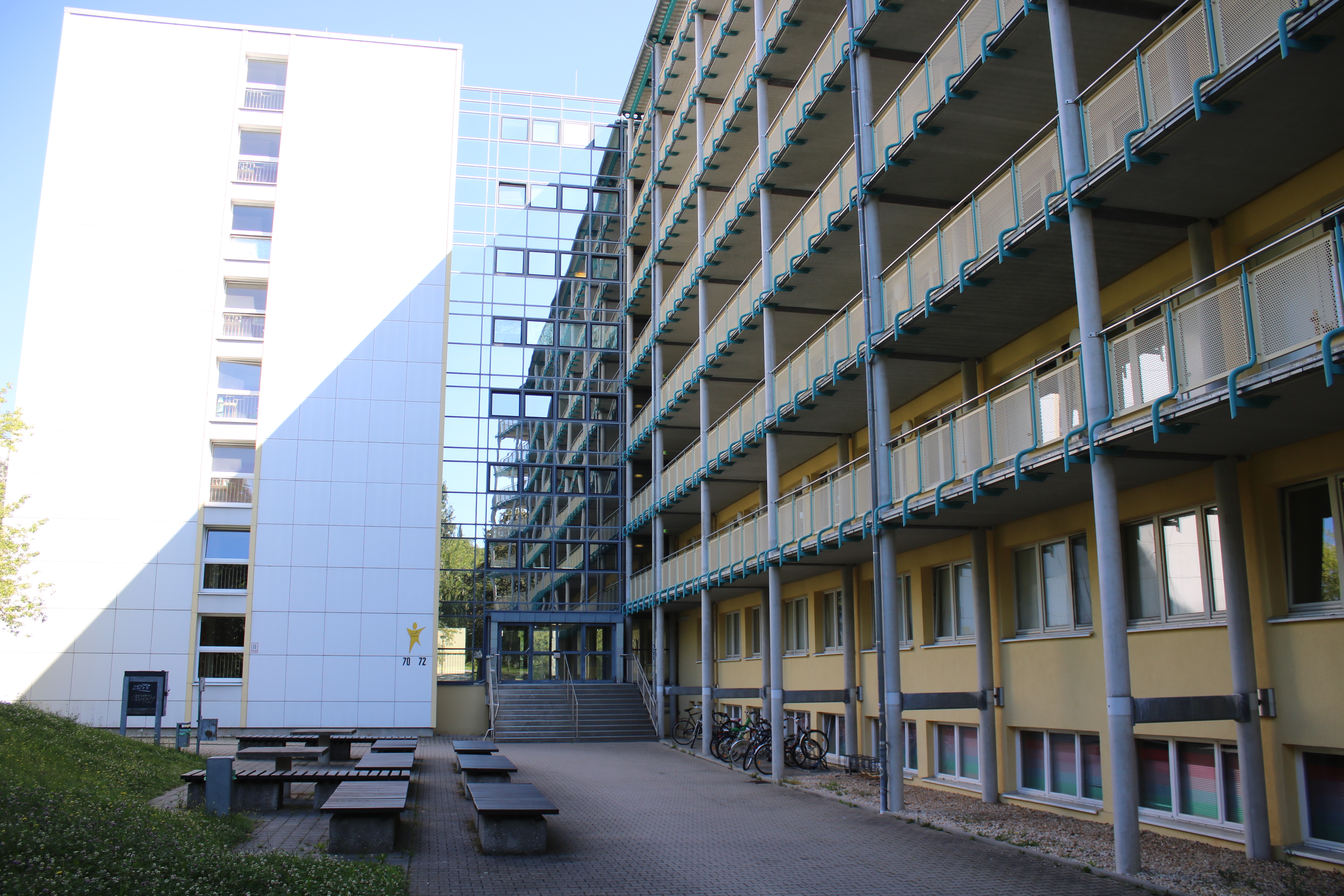 Wohnheimansicht, Glasfassade beim Eingang, Balkonbogengang um das Gebäude, Bänke vor Wohnheim