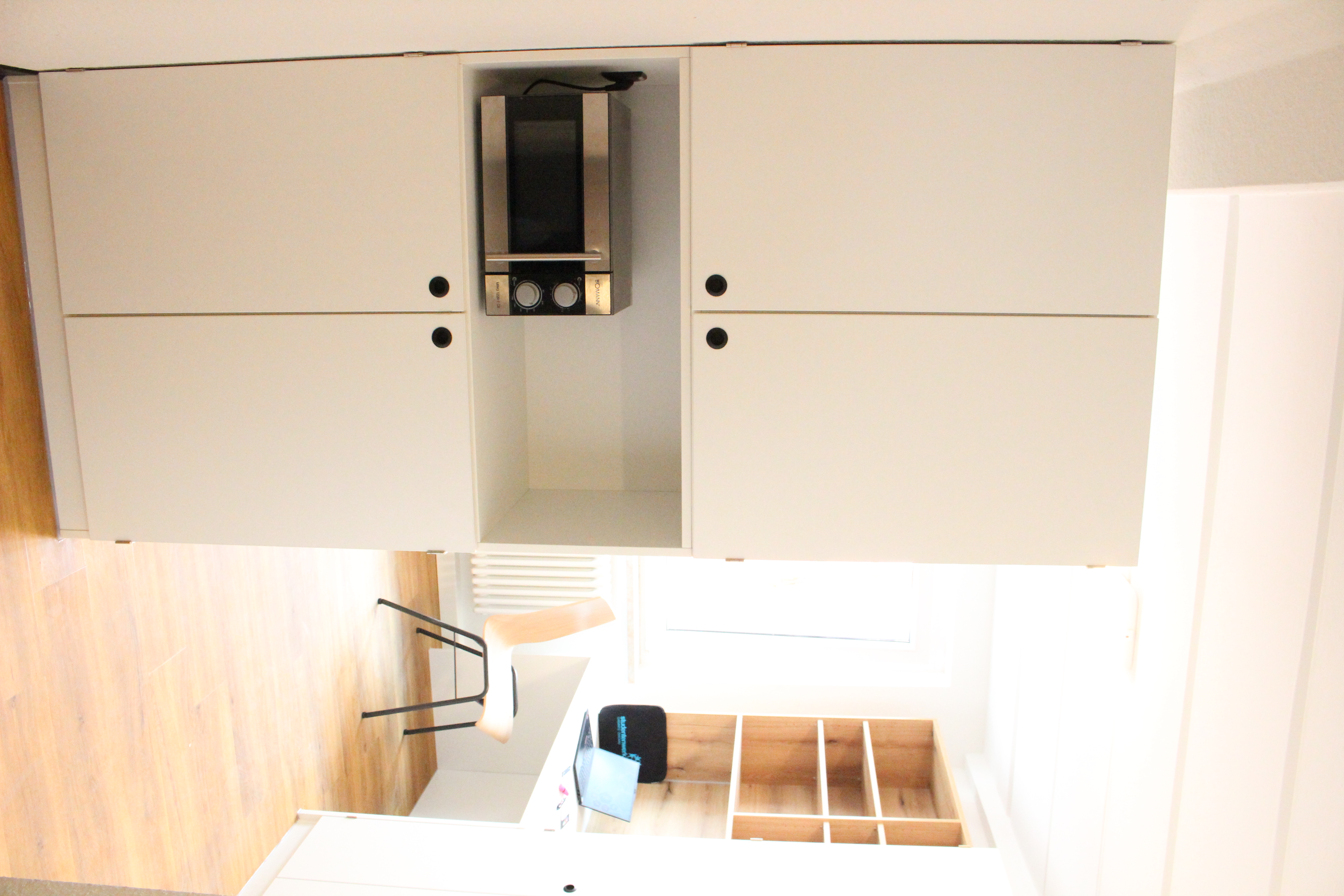 Großer weißer Schrank, Mikrowelle, Schreibtisch mit Stuhl und Laptop